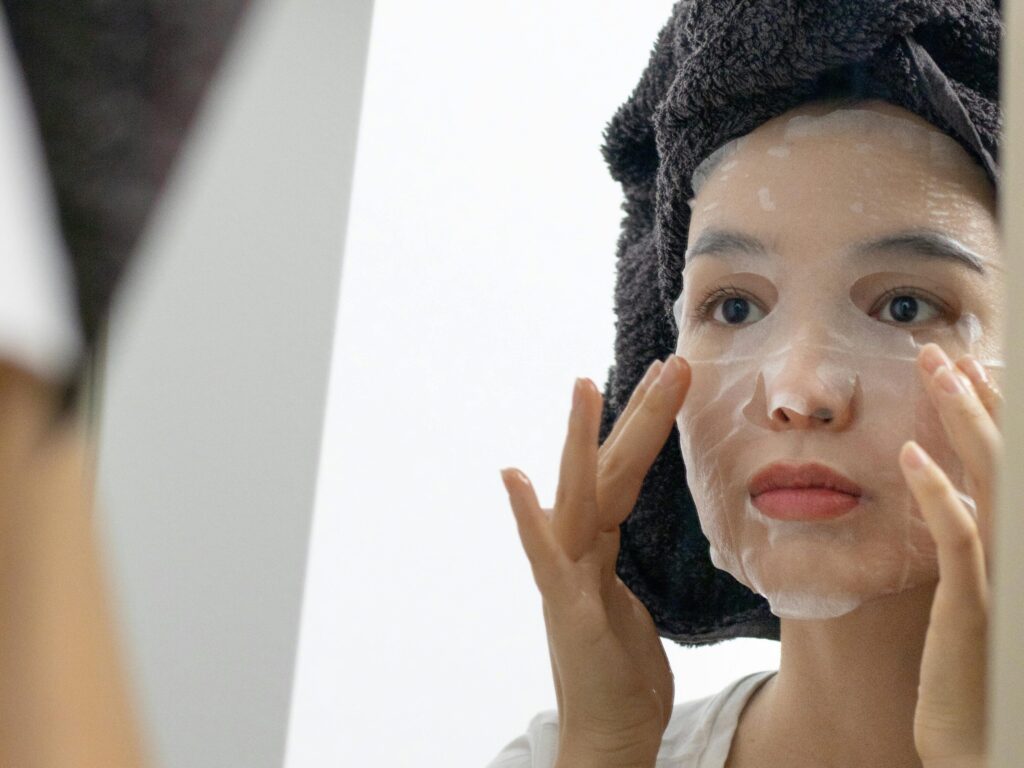 pexels photo 6925516 6925516 Woman applies a skincare sheet mask in front of a mirror, focusing on self-care and facial treatment.